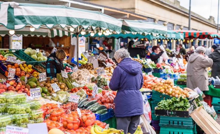 Customers looking at fruit and veg for sale whilst stall holders are selling it to them